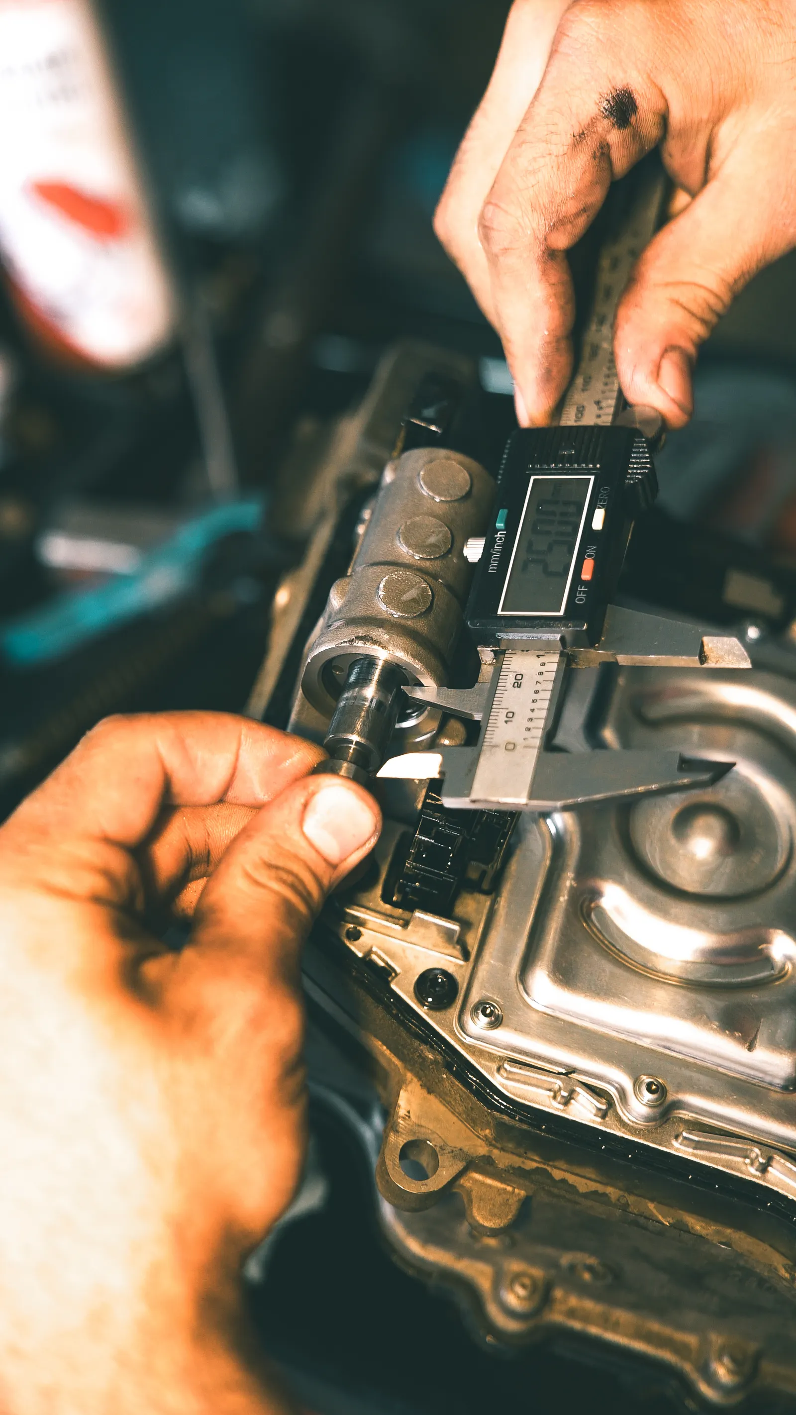 A machinist measures a metal component with a digital caliper